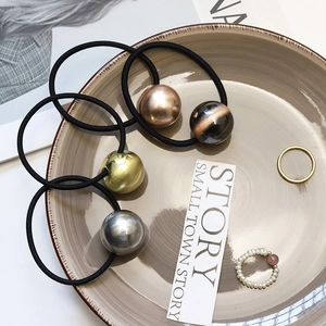 Detailed view of four elastic hair ties with brushed metallic spheres in a ceramic tray