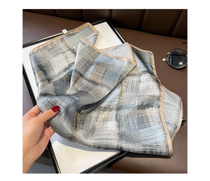 Dettaglio di un foulard in seta a righe grigio-blu con eleganti bordi beige rifiniti