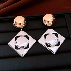 Macro shot of geometric mixed-metal earrings with gold studs and silver diamond frames