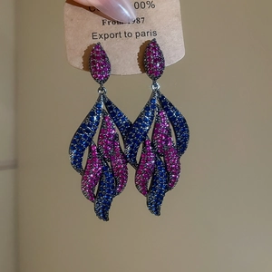 Detail of drop earrings with pink and blue rhinestones on black metal leaves