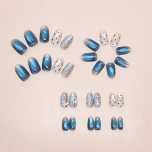 Detail of blue cat eye press-on nails with plaid patterns and 3D white bows accents