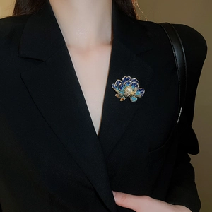 Detailed shot of a blue enamel flower brooch with a white pearl on a black suit jacket