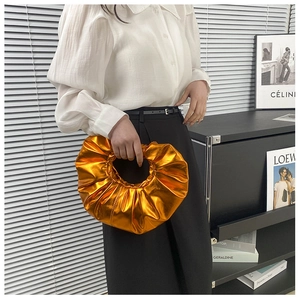 Detailaufnahme einer metallisch-orangen Plissee-Ringhandtasche, gehalten von einem Modell