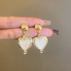 Detail of vintage heart-shaped gold earrings with white resin and pavé stone accents