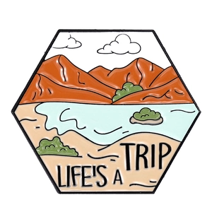 Macro detail of enamel pin showing mountains, lake scenery and Life's A Trip slogan