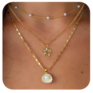 Detailed close-up of layered gold necklace with shell and pearl charms on a model