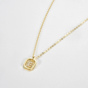 Macro detail of S925 silver necklace featuring a gold pendant with a jeweled letter E