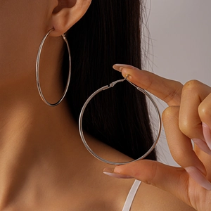 Close-up of a model wearing large silver geometric hoop earrings with polished metal finish