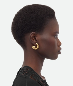 Detail of chunky gold-plated stainless steel twisted hoop earring on model's ear