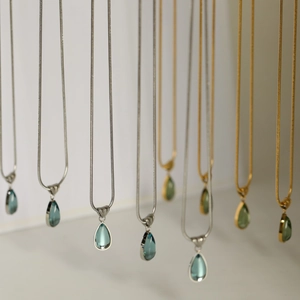 Close-up of waterdrop pendants in ocean blue and olive green on sleek snake chains