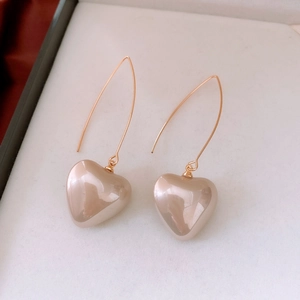Détail de boucles d'oreilles cœur dorées avec longs crochets sur fond à texture douce