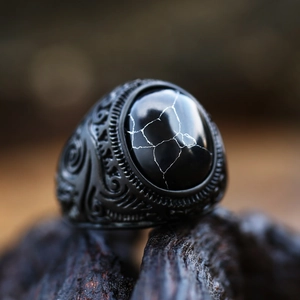 Vista macro di un anello retrò in acciaio nero con motivi incisi e gemma nera intarsiata