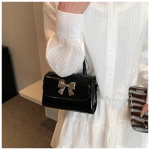 Dettaglio di una borsa a mano in vernice nera con un grande fiocco in metallo argento sulla tracolla