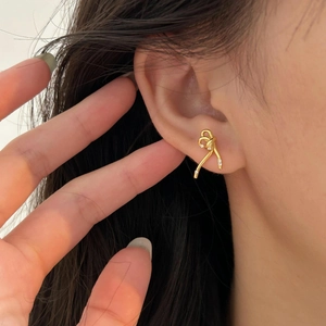 Close-up of a gold ribbon bow earring with small zircons worn on a model's ear