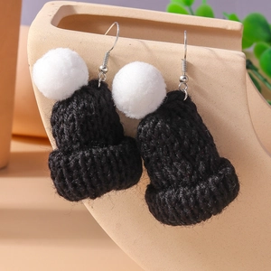 Handmade black knit hat earrings with white fluffy pompoms on a minimalist display