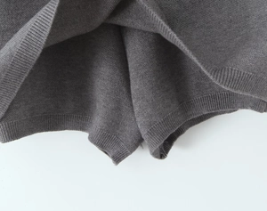 Detail of dark grey knit skirt showing ribbed hemline and fine fabric texture on white background