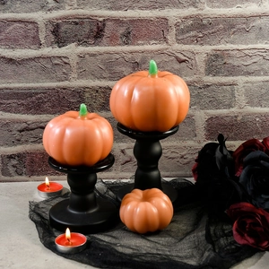 Tre candele a forma di zucca arancione di diverse dimensioni su candelieri neri