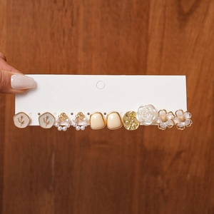 Close-up of five pairs of resin pearl and flower stud earrings on white display card