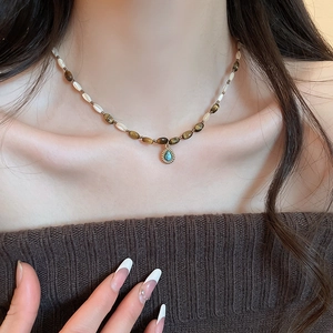 Detail of beaded tiger eye necklace with turquoise pendant on woman's collarbone