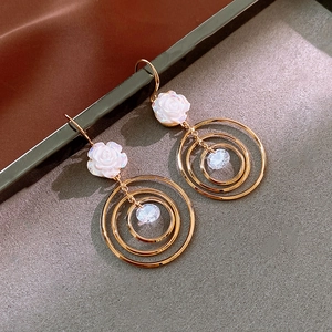 Détail de boucles d'oreilles roses avec cercles dorés et pétales blancs sur tissu