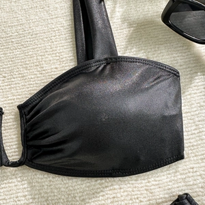 Detail of black metallic bikini top with shimmering texture and ruched side on white fabric
