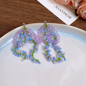 Detail of handmade beaded flower tassel earrings in purple and green with silver pins