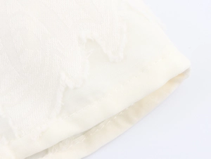 Close-up detail of white long sleeve blouse with ruffled edges and textured jacquard fabric