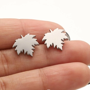 Macro detail of silver maple leaf stud earrings made of polished stainless steel on finger