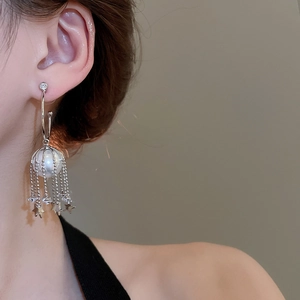 Detail of star tassel pearl earrings featuring a large pearl and hanging metal chains