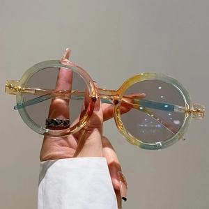 Détail de lunettes de soleil rondes avec verres dégradés jaune-vert en main