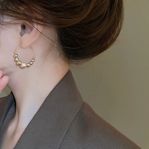 Detail of twisted gold hoop earring with mixed pearls worn by a model in profile