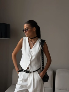 Detail view of white V-neck vest with white buttons and matching straight trousers