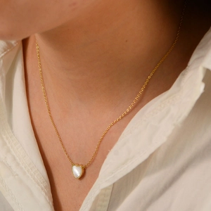 Close-up of a heart-shaped white shell pendant on a gold necklace worn by a model