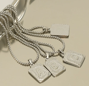 Macro shot of silver square letter pendants A, B, and C on round box chains