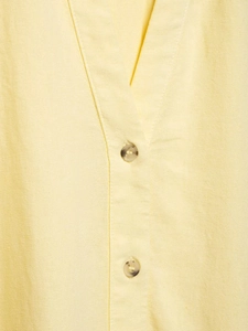 Detail of pale yellow linen-blend shirt featuring V-neckline and tortoiseshell buttons