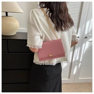 Pink quilted crossbody bag with gold chain strap shown on model in modern home setting
