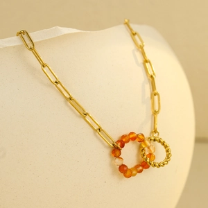 Macro shot of gold paperclip chain necklace with interlocking orange bead and twisted ring