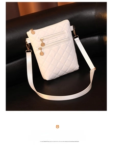 Detail of white quilted crossbody bag featuring three front zippers with gold round pulls