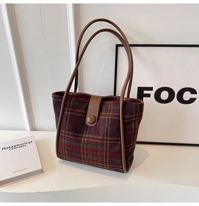 Detail of red and green plaid tote bag with brown leather handles in a minimalist room