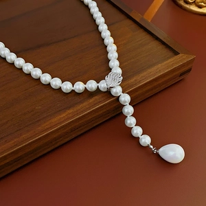 Detail of zircon leaf clasp and teardrop pearl pendant on a polished pearl necklace