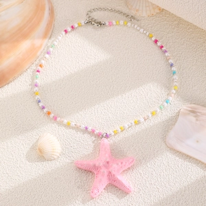 Detail of pink starfish pendant on colorful beaded necklace with sea shells background