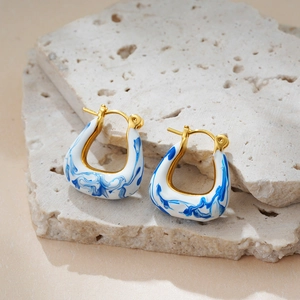 Detailed shot of 18K gold earrings with blue and white enamel glaze on a stone base