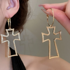 Detailed view of large gold hoop earring with textured cross pendant and embossed metal surface