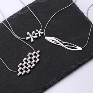 Détail de trois pendentifs fleur en argent avec chaînes serpent sur support en ardoise noire