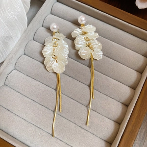 Detail of white petal earrings with long gold tassels and pearl studs in jewelry box