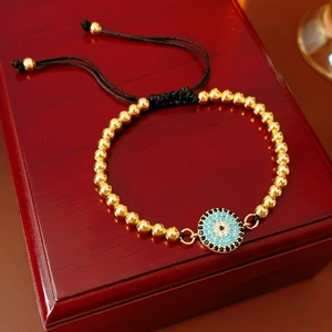Détail de bracelet à billes dorées avec breloque œil bleu et cordon ajustable