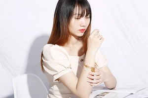 Detail of a gold zodiac bracelet with a Leo pendant worn by a model on a white fabric