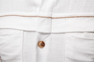 Detail of white linen-blend shirt showing wavy brown stitching and amber button texture