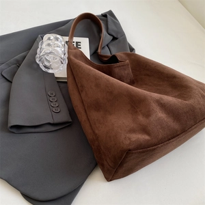Close-up of a large dark brown suede tote bag placed elegantly on a grey business blazer