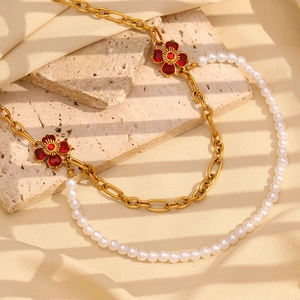 Detail of necklace with gold chain, white pearls and red flower charms on stone